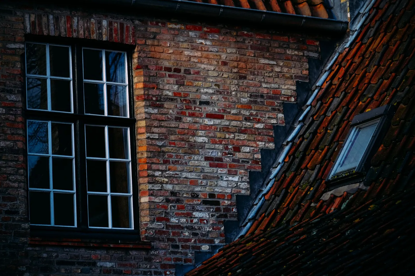 A detailed view of a brick building's facade with two windows on a sunny day.